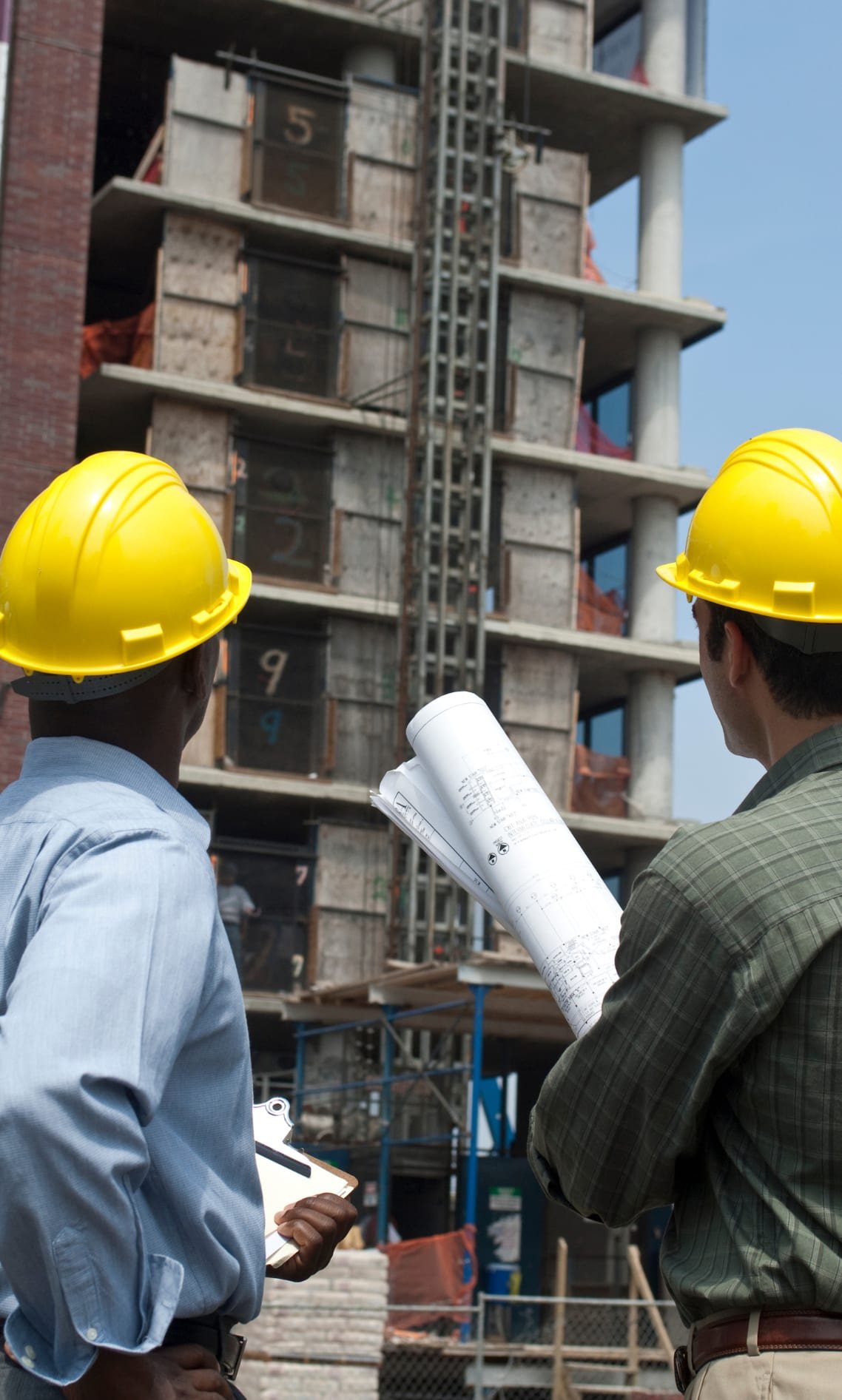 Two engineers in hard hats reviewing project drawings on site
